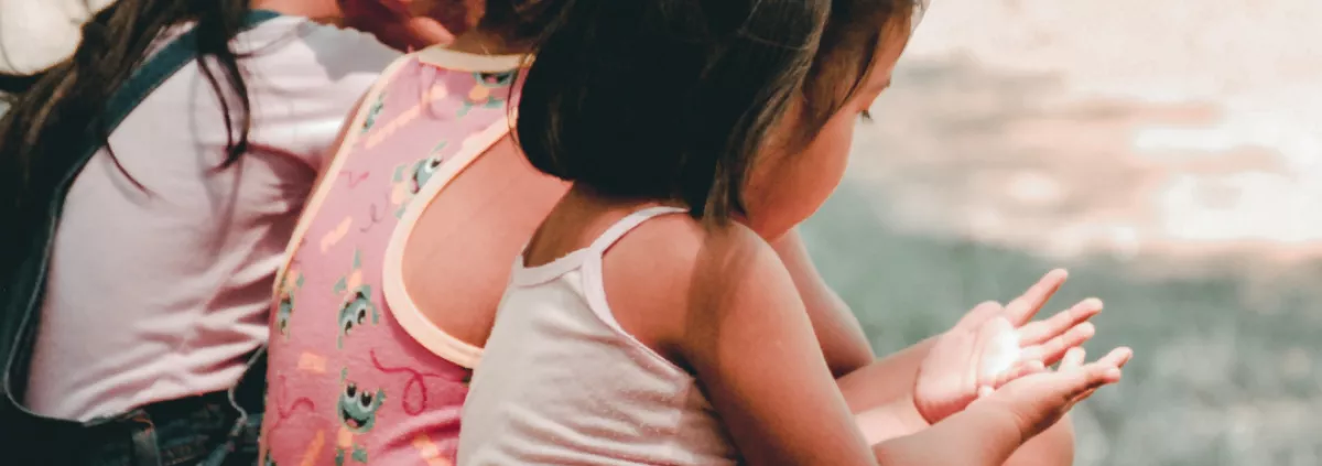 text: Reiki for Kids. Children sitting on a hillside looking at sun on hands. 